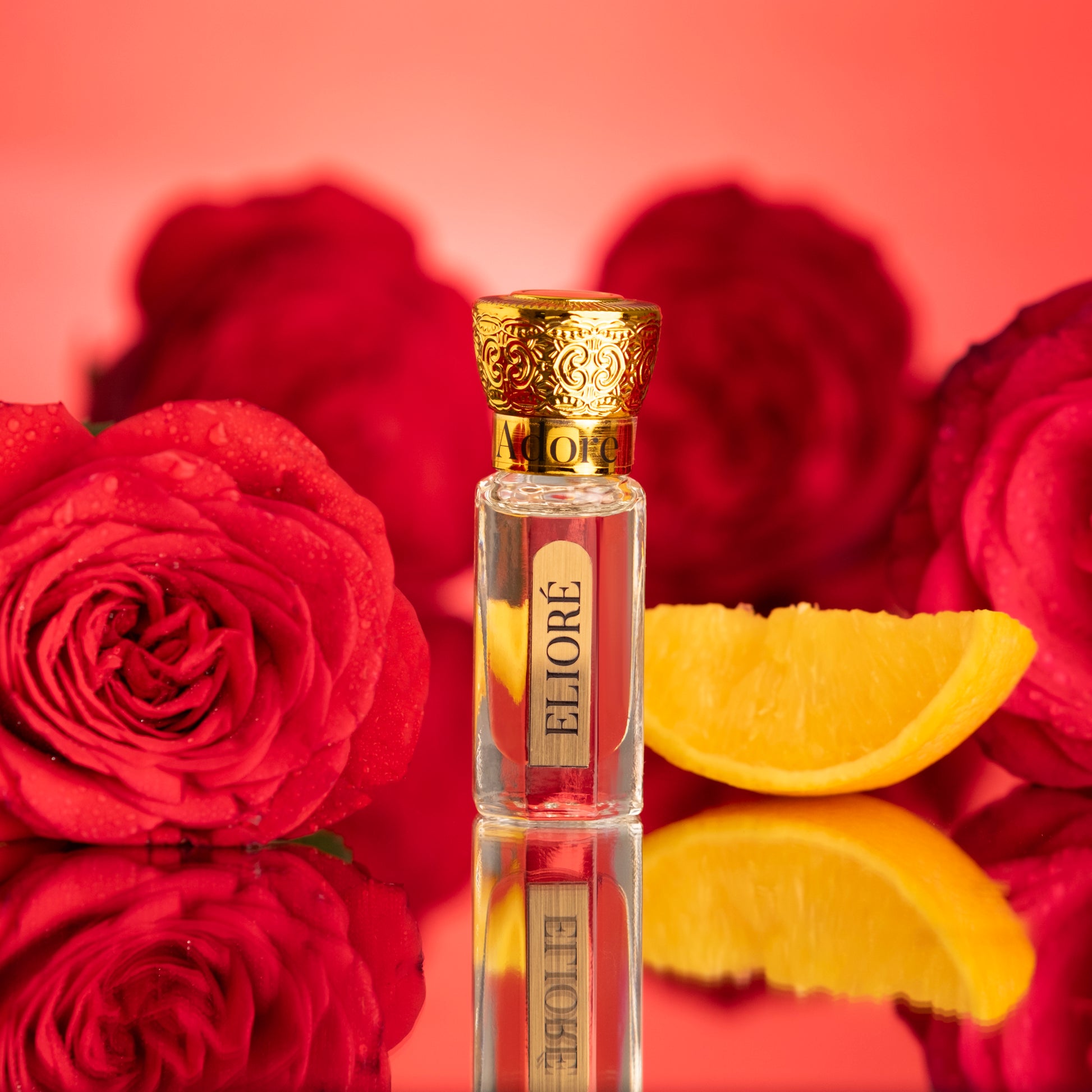 Adore by Elioré luxury attar perfume bottle surrounded by fresh roses and citrus slices in an elegant floral fragrance photoshoot.