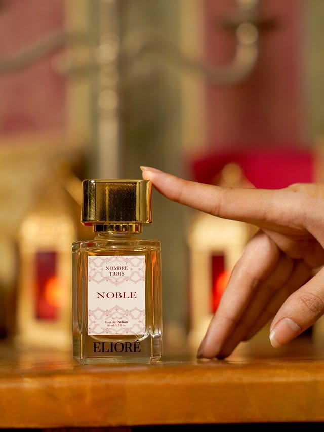 Perfume bottle labeled 'Noble' by Eliore held by a hand with a blurred background