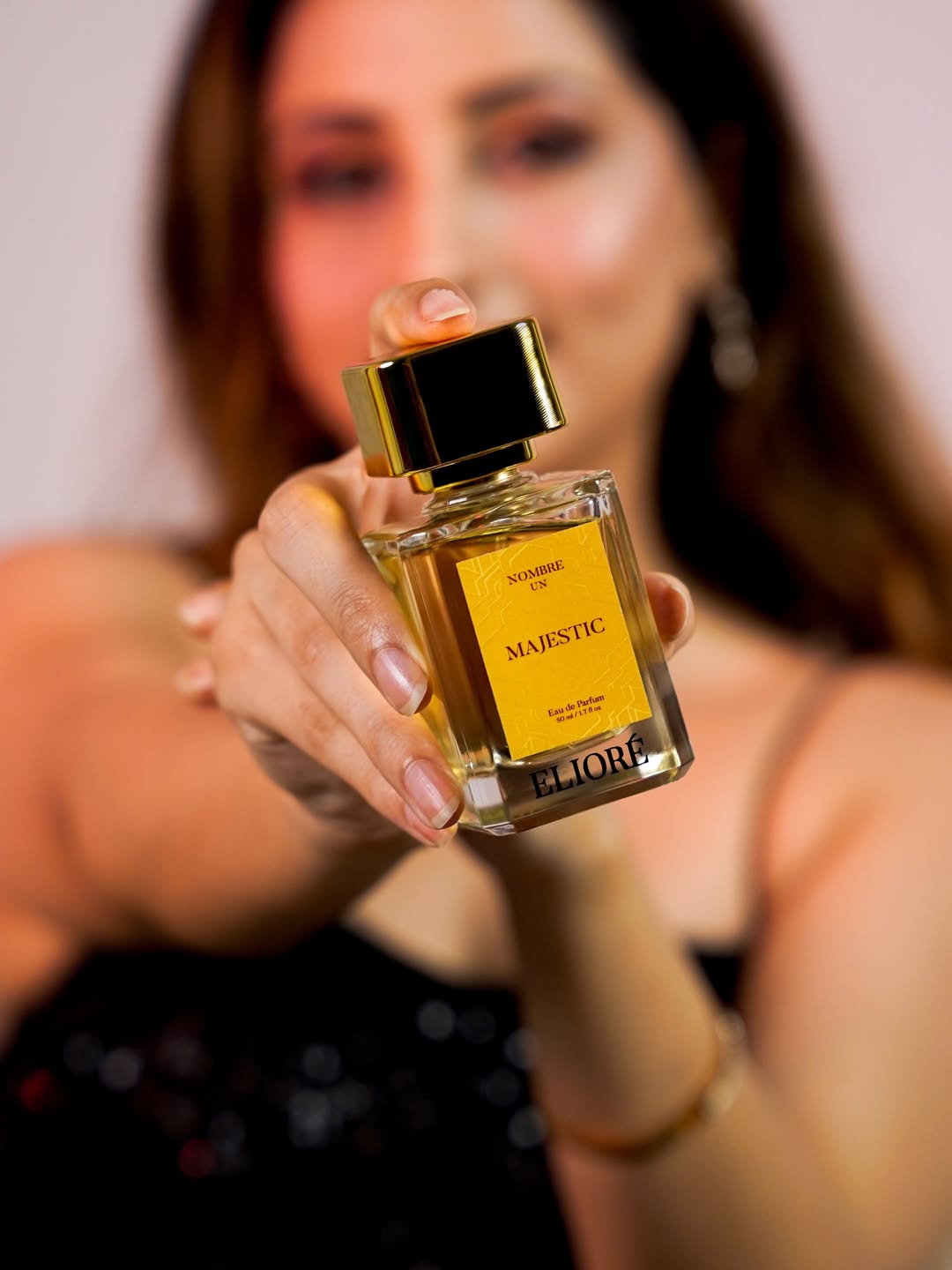 Woman holding a bottle of 'Majestic' perfume by Eliore against a blurred background