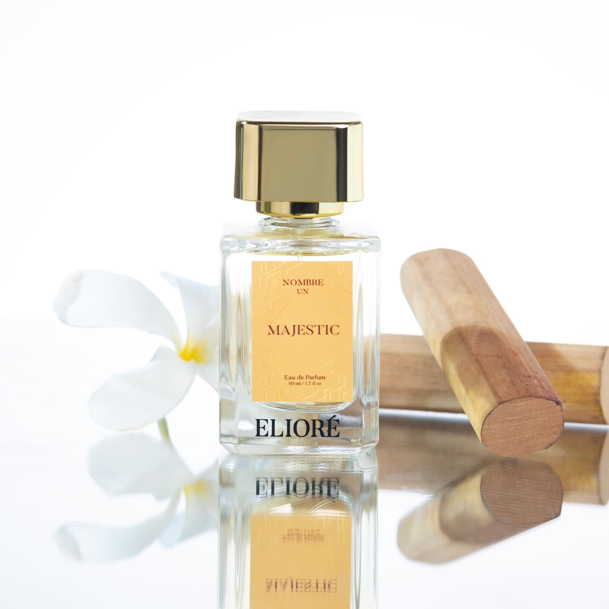 Perfume bottle labeled 'Majestic' by Eliore with a wooden roller and white flowers on a reflective surface.