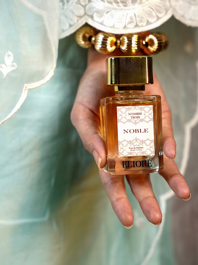 Perfume bottle labeled 'Noble' held in a hand with a decorative background