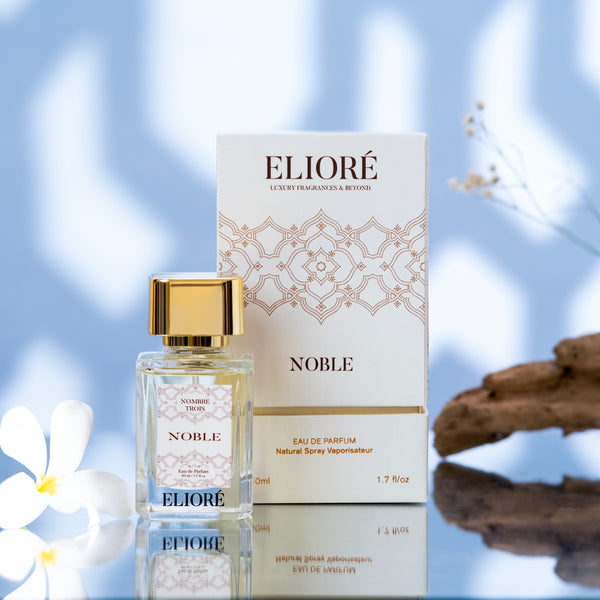 Eliore Noble perfume bottle and packaging on a reflective surface with a blurred floral background