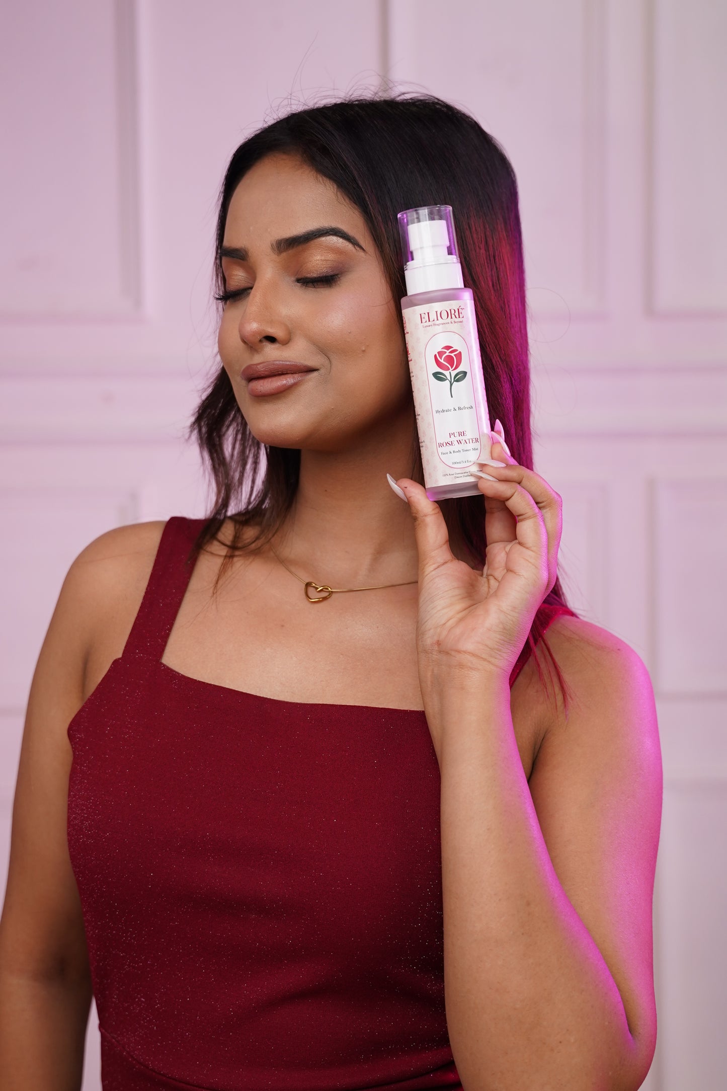 Woman holding a eliore pure rose water with a pink background