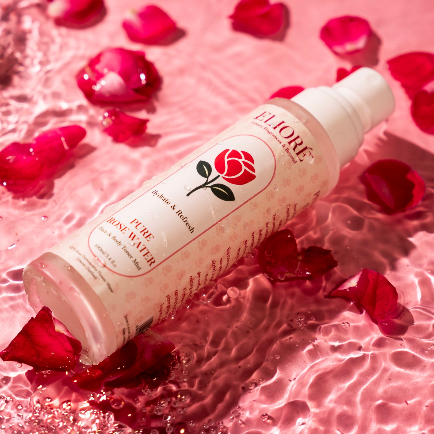 Pure Rose Water Mist by Elioré Essentials floating in pink water with scattered rose petals in a luxurious hydrating skincare photoshoot.