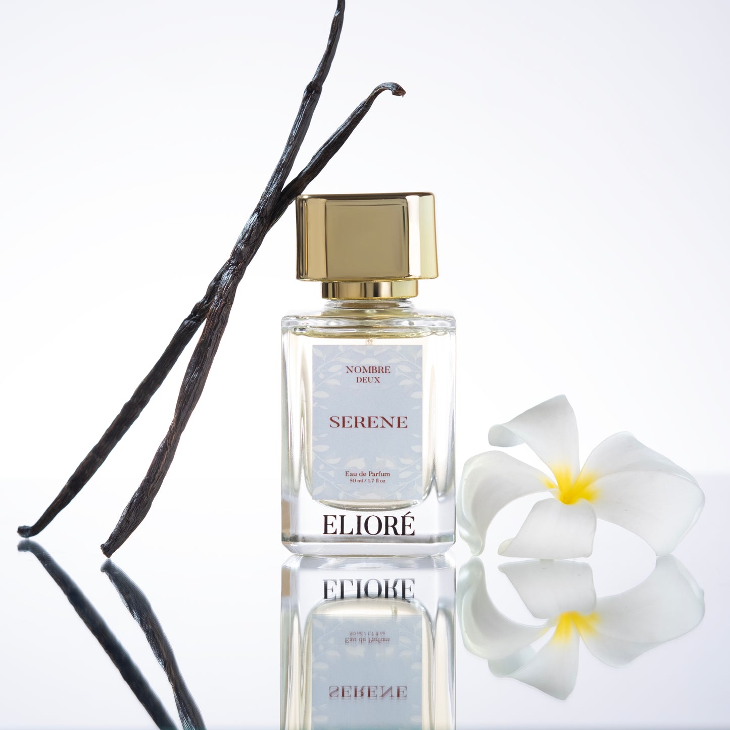 Perfume bottle labeled 'Eliore' with vanilla bean and flower on a reflective surface