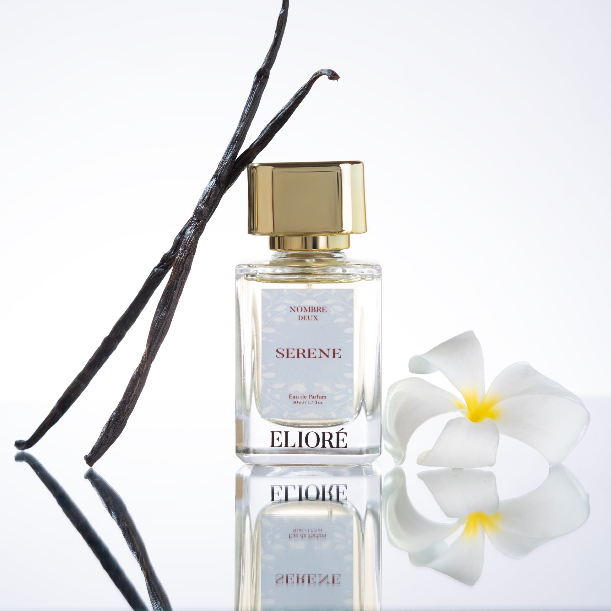 Perfume bottle labeled 'Eliore' with vanilla bean and flower on a reflective surface