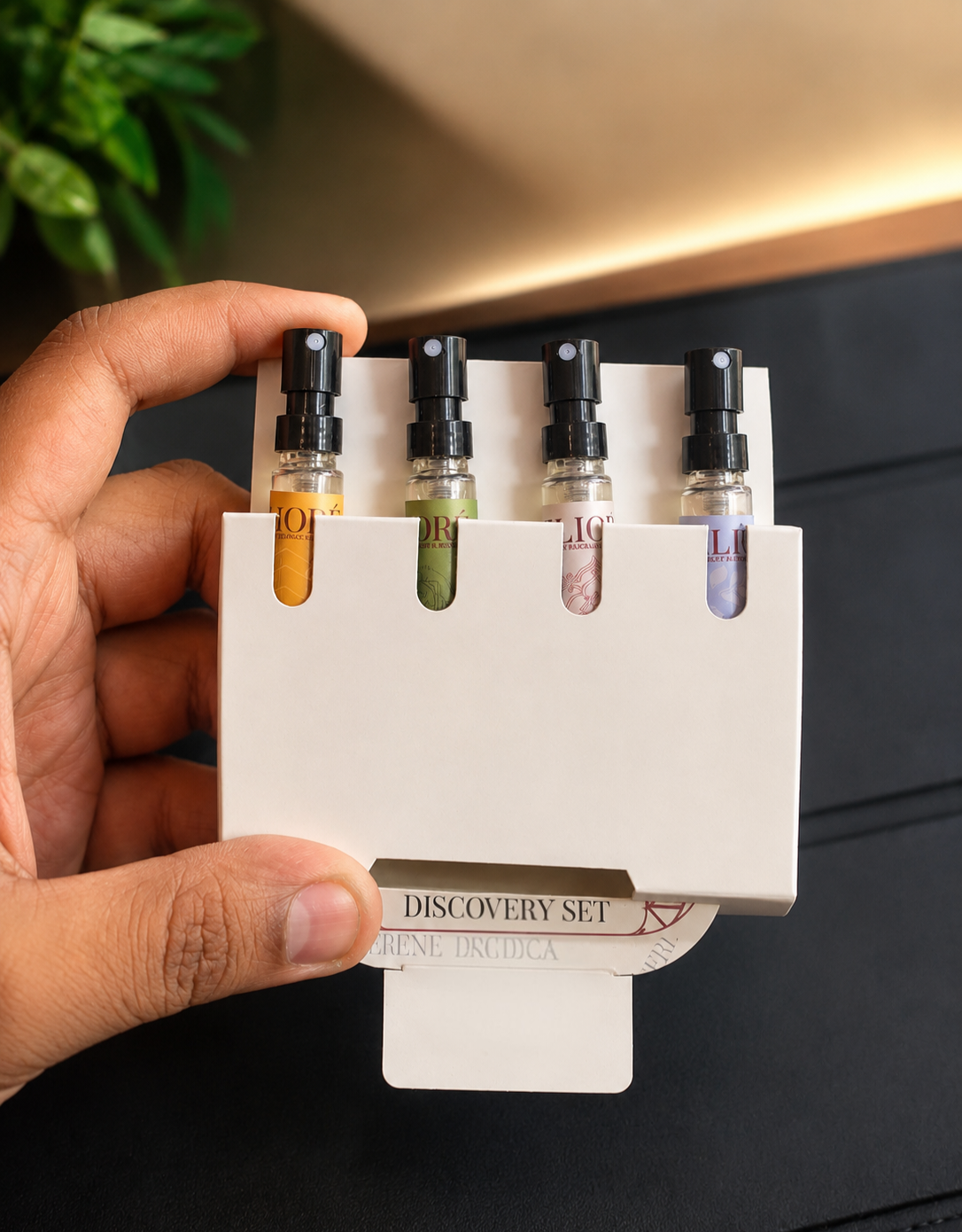 Hand holding a small white stand with four small bottles of different colors, labeled 'Eliore Discovery Set'.