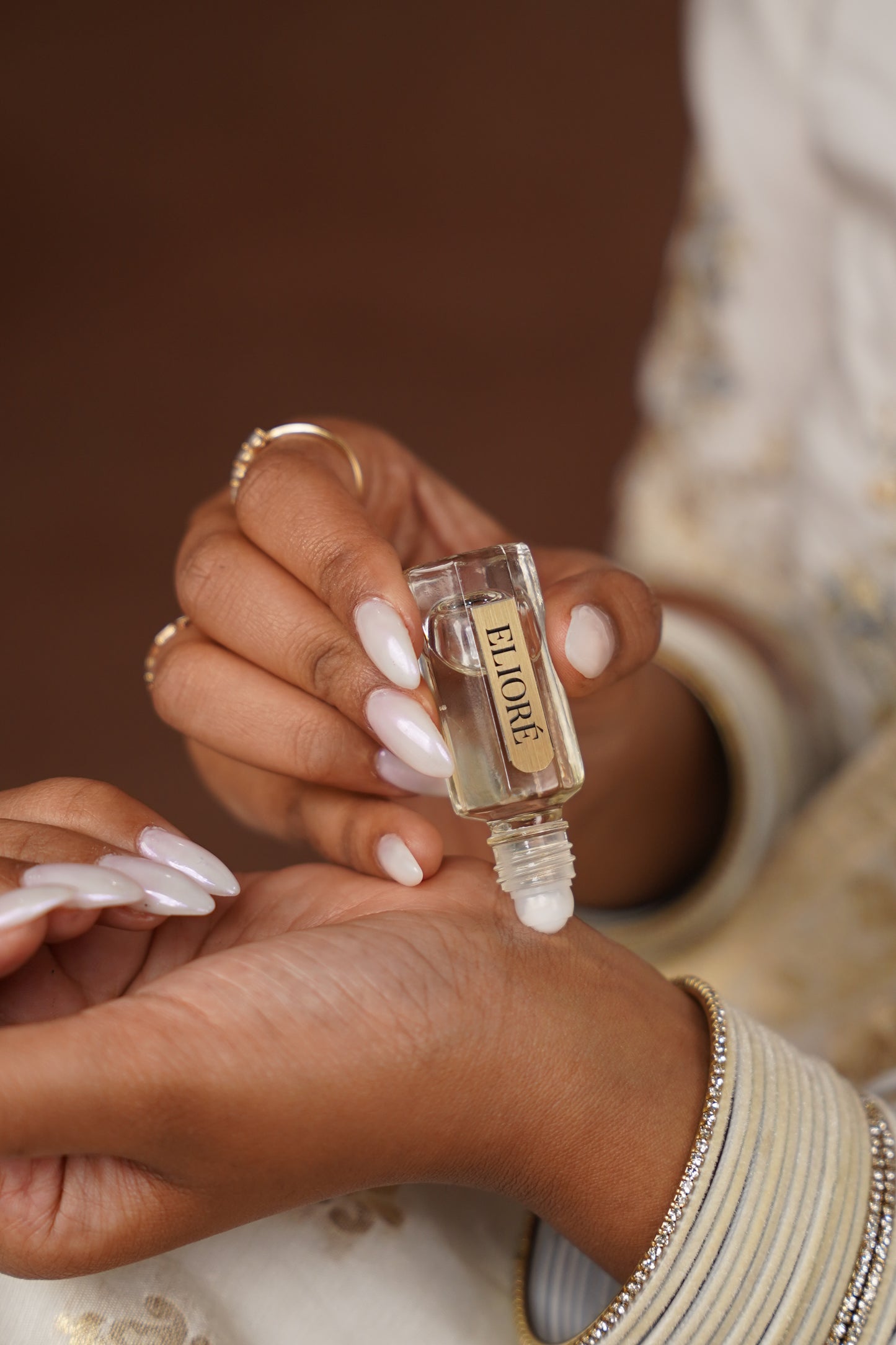Hand holding a small perfume bottle with 'Eliore' branding against a blurred background